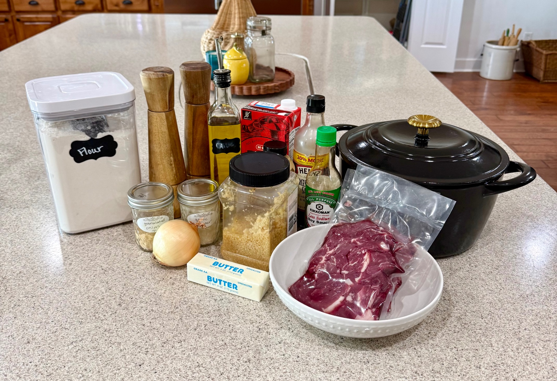 Beef tips ingredients and a Dutch oven arranged on the kitchen counter, including stew meat, onion, garlic, butter, flour, beef broth, oil, Worcestershire sauce, and soy sauce.