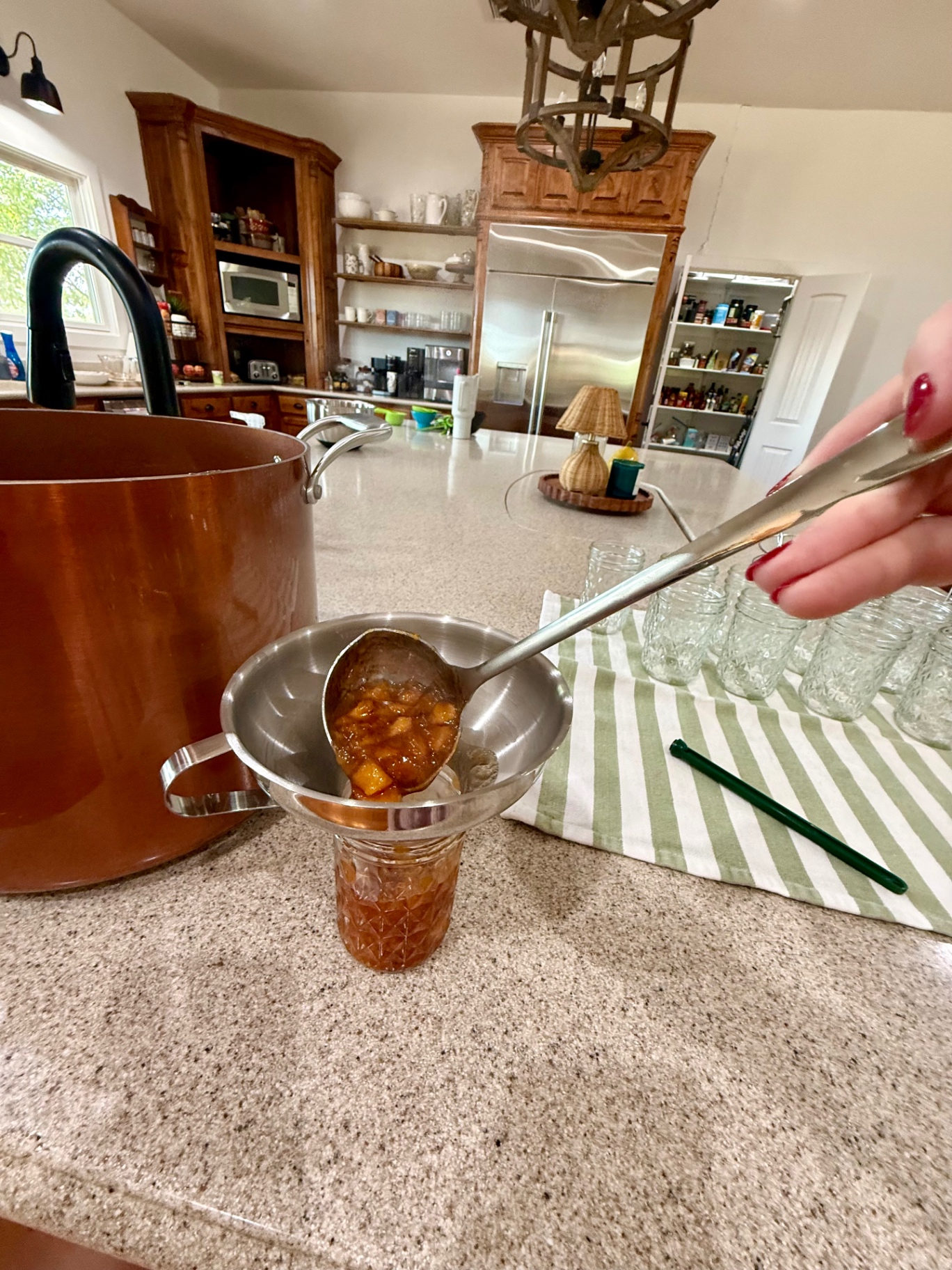 Hot peach topping being ladled through a canning funnel into a half-pint jar