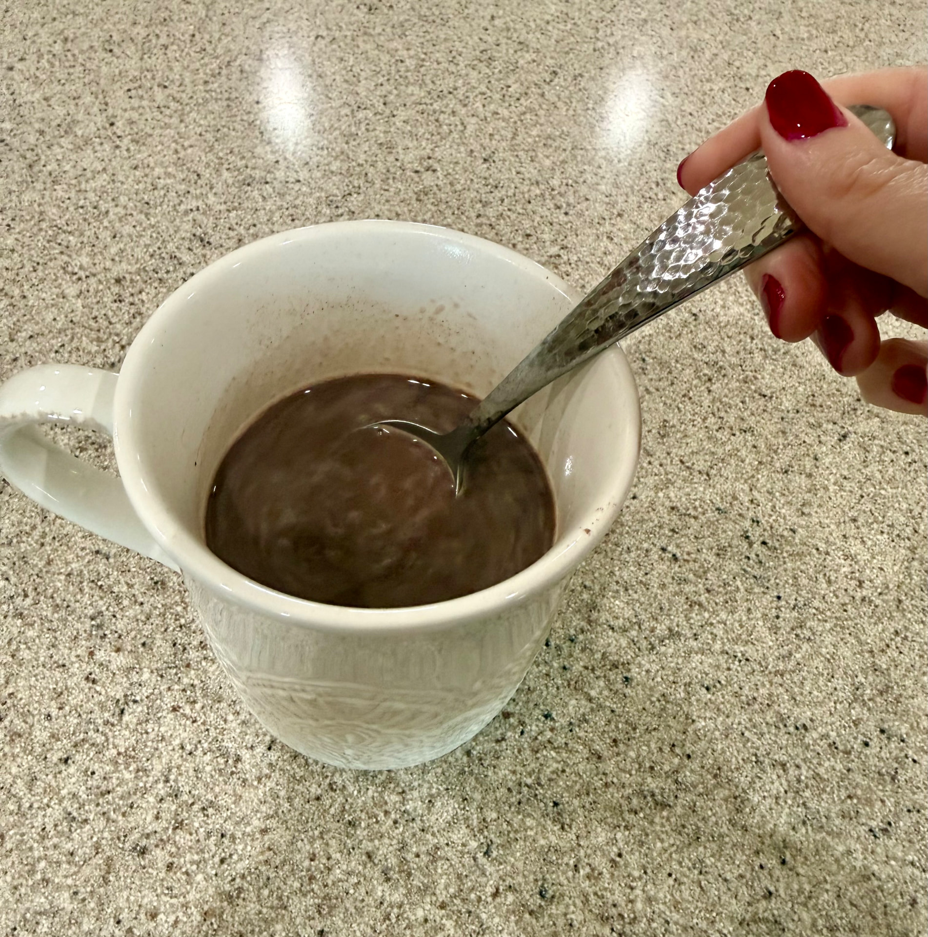 Stirring hot cocoa smooth with a spoon in a white mug.