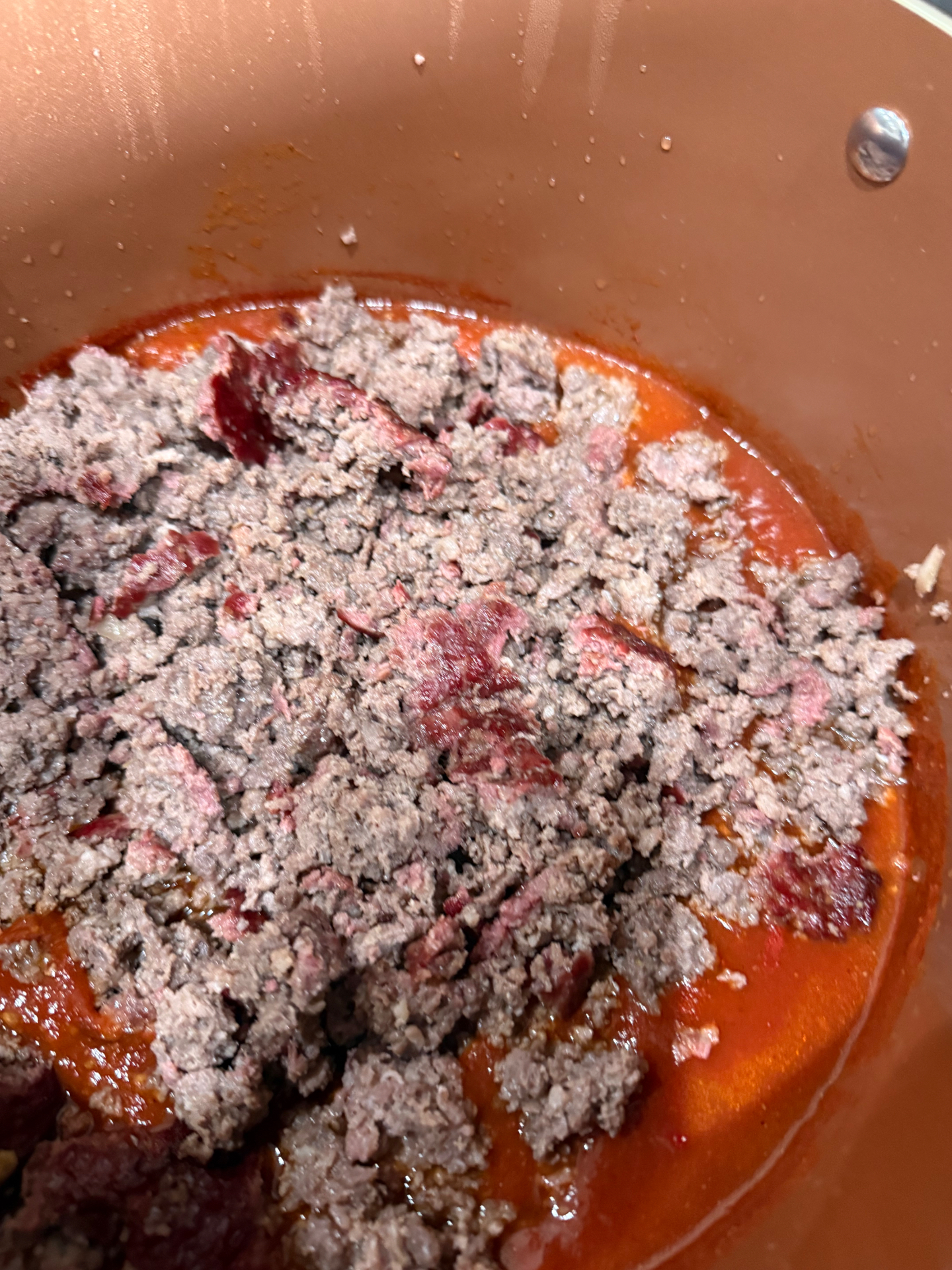 Crumbled smoked ground beef stirred into red chili base in a Dutch oven