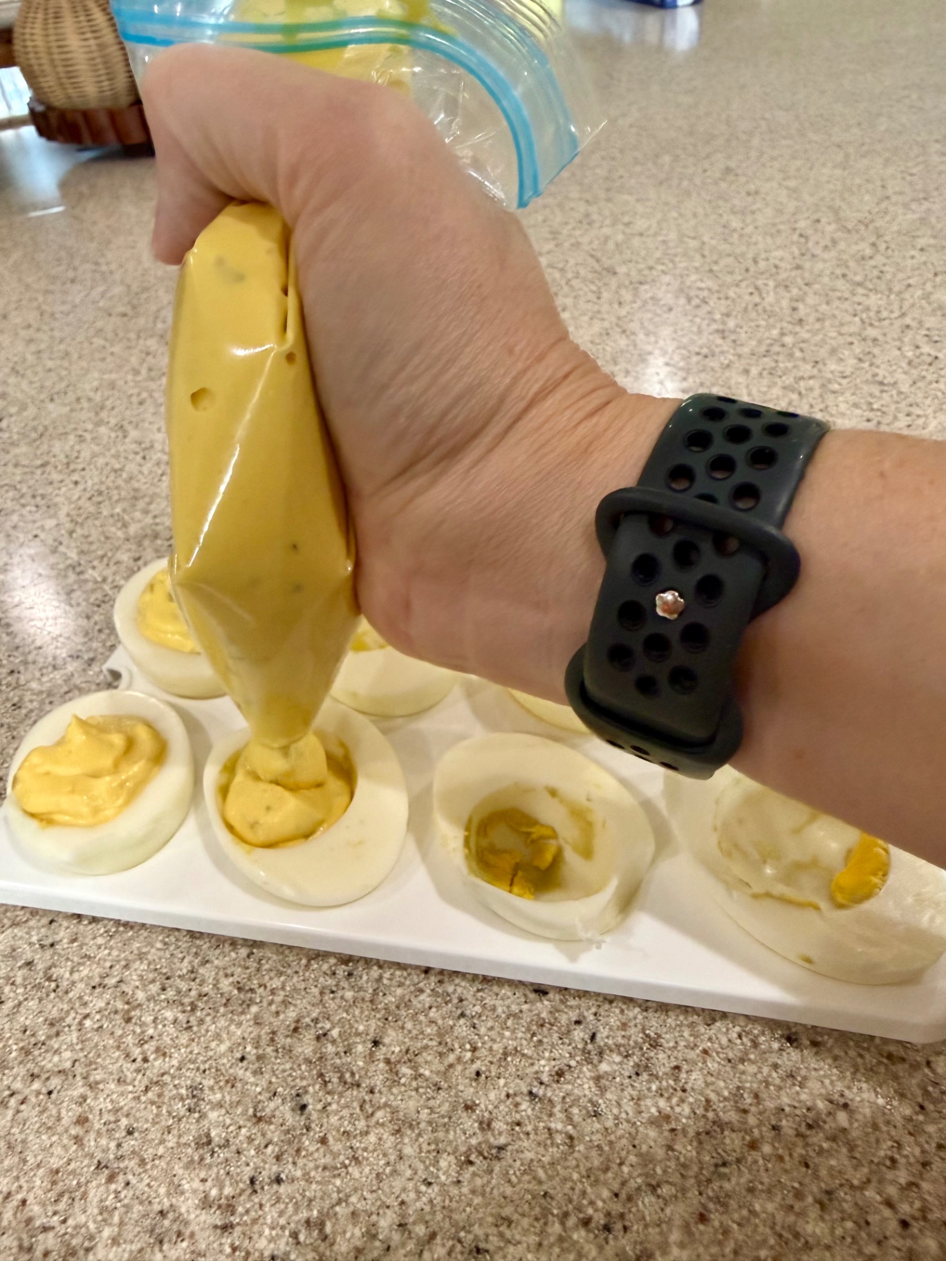Piping deviled egg filling from a zip-top bag into egg white halves on a serving tray.