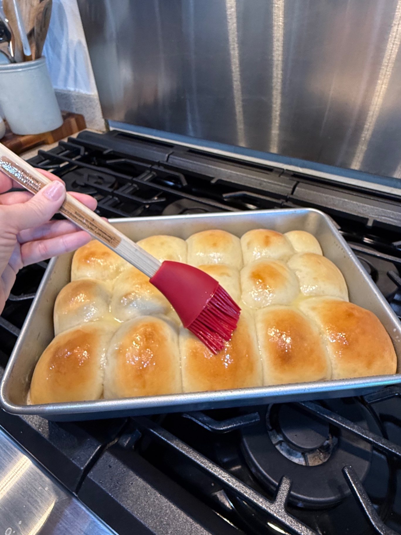 Brushing hot golden dinner rolls with melted butter using a red pastry brush.