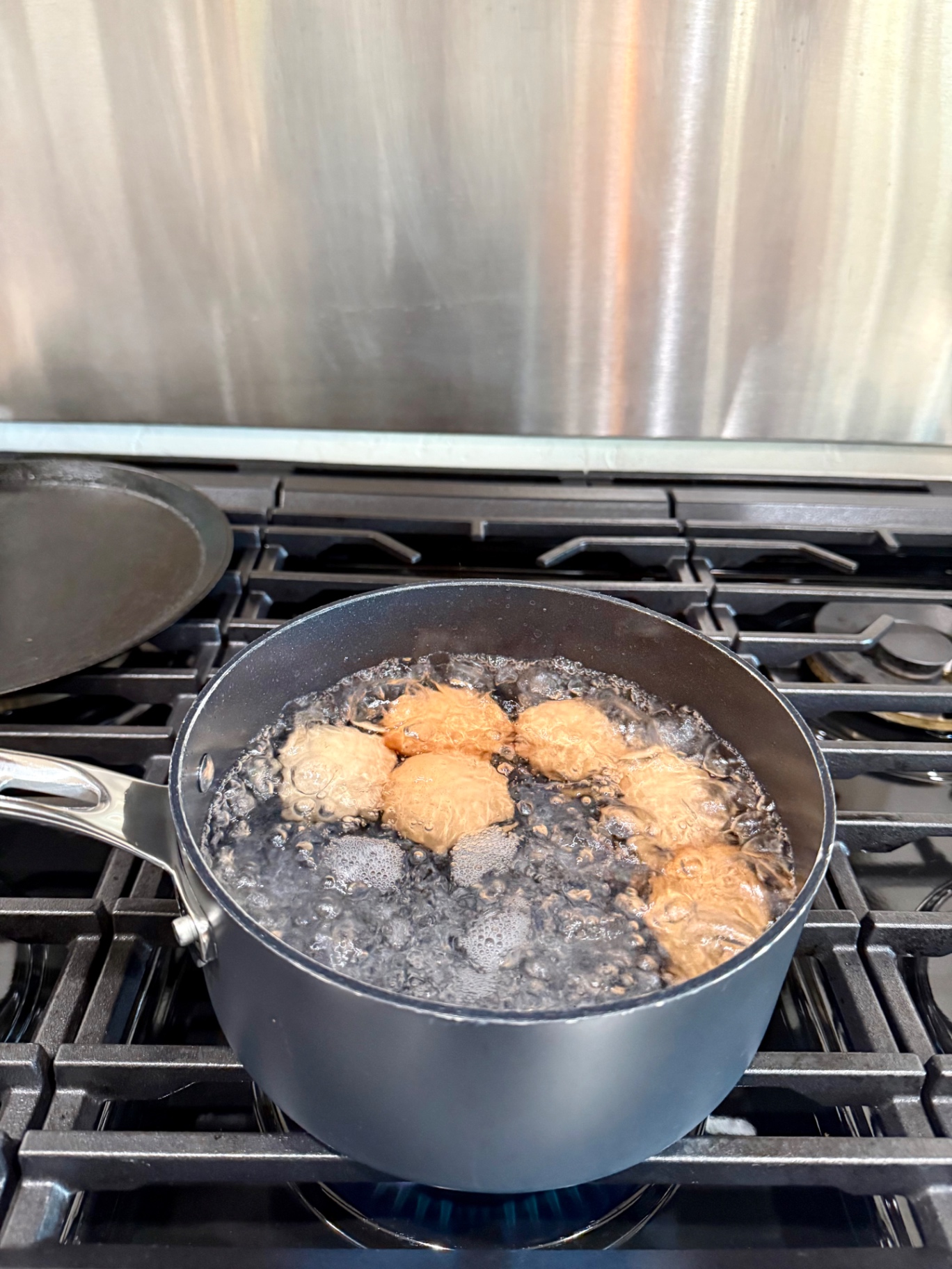 Brown eggs boiling in a saucepan of water on the gas stove.
