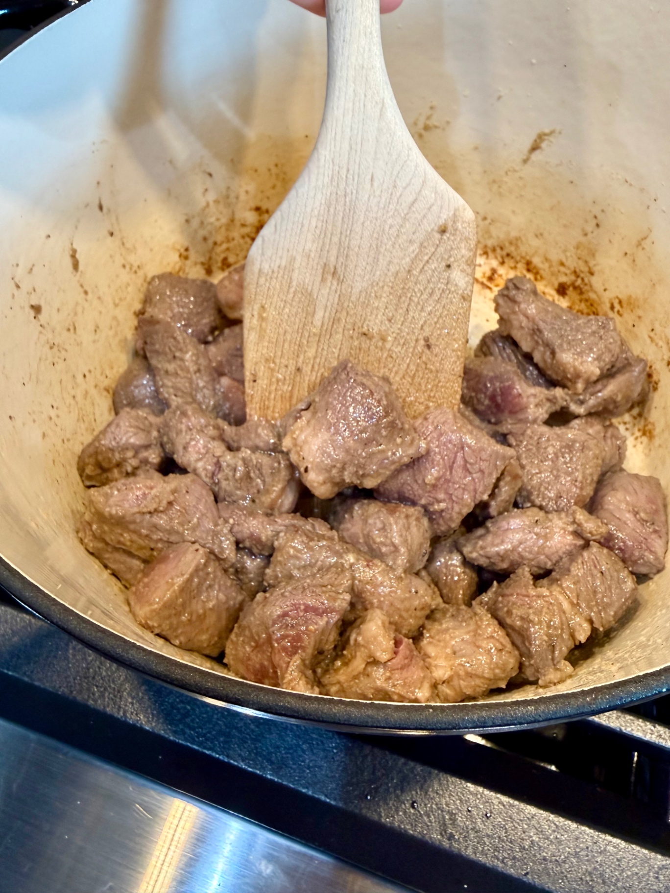 Browned beef pieces in an enameled Dutch oven with a wooden spoon.