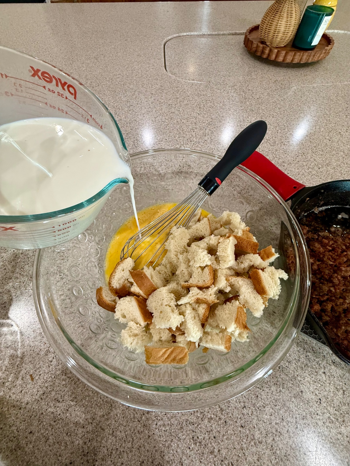 Milk being poured from a glass measuring cup into a bowl of beaten eggs and torn bread pieces