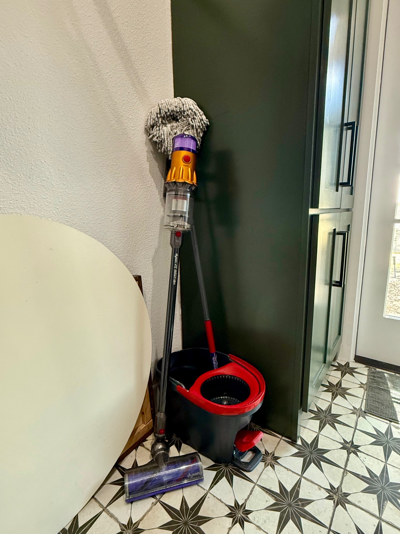 Mop stored upside down to dry next to a cordless vacuum and spin mop bucket in a corner