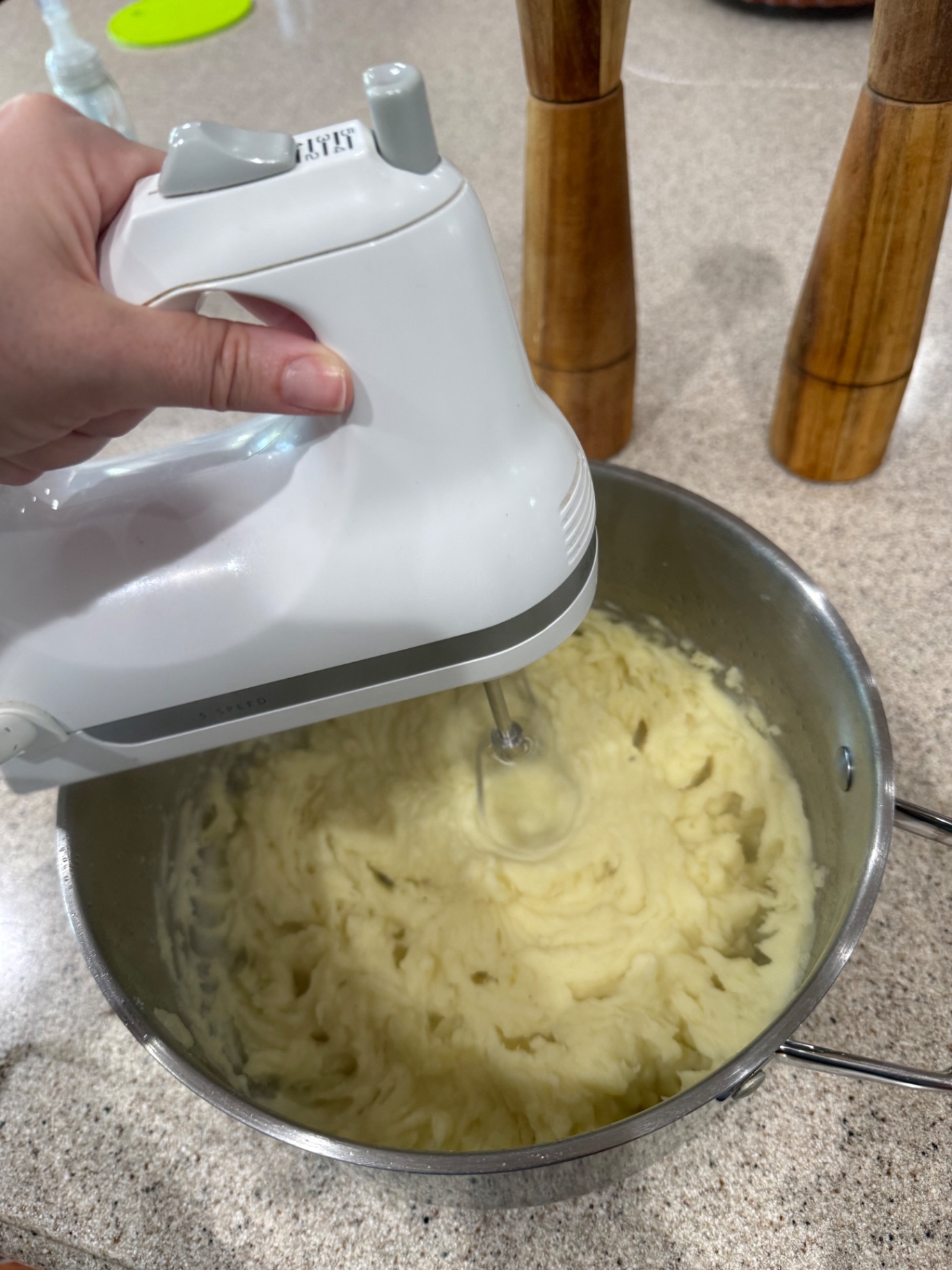 A white hand mixer mixing mashed potatoes in the pot on the kitchen counter.