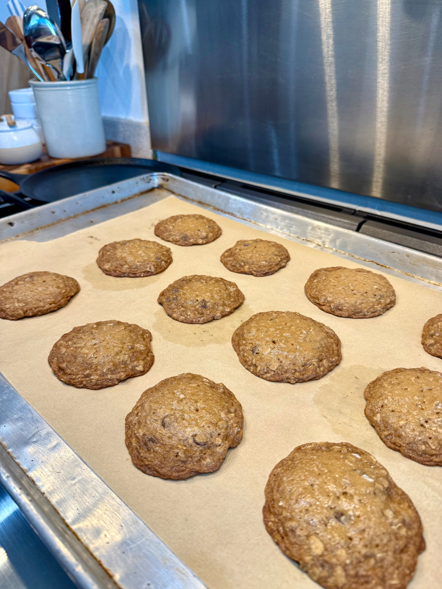 Freshly baked oatmeal cookies on a parchment-lined baking sheet beside the stove.