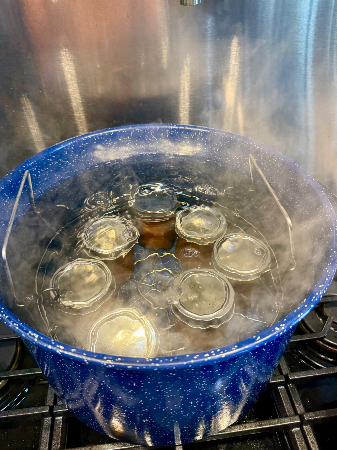 Jars of peach topping submerged in a blue water-bath canner at a full rolling boil