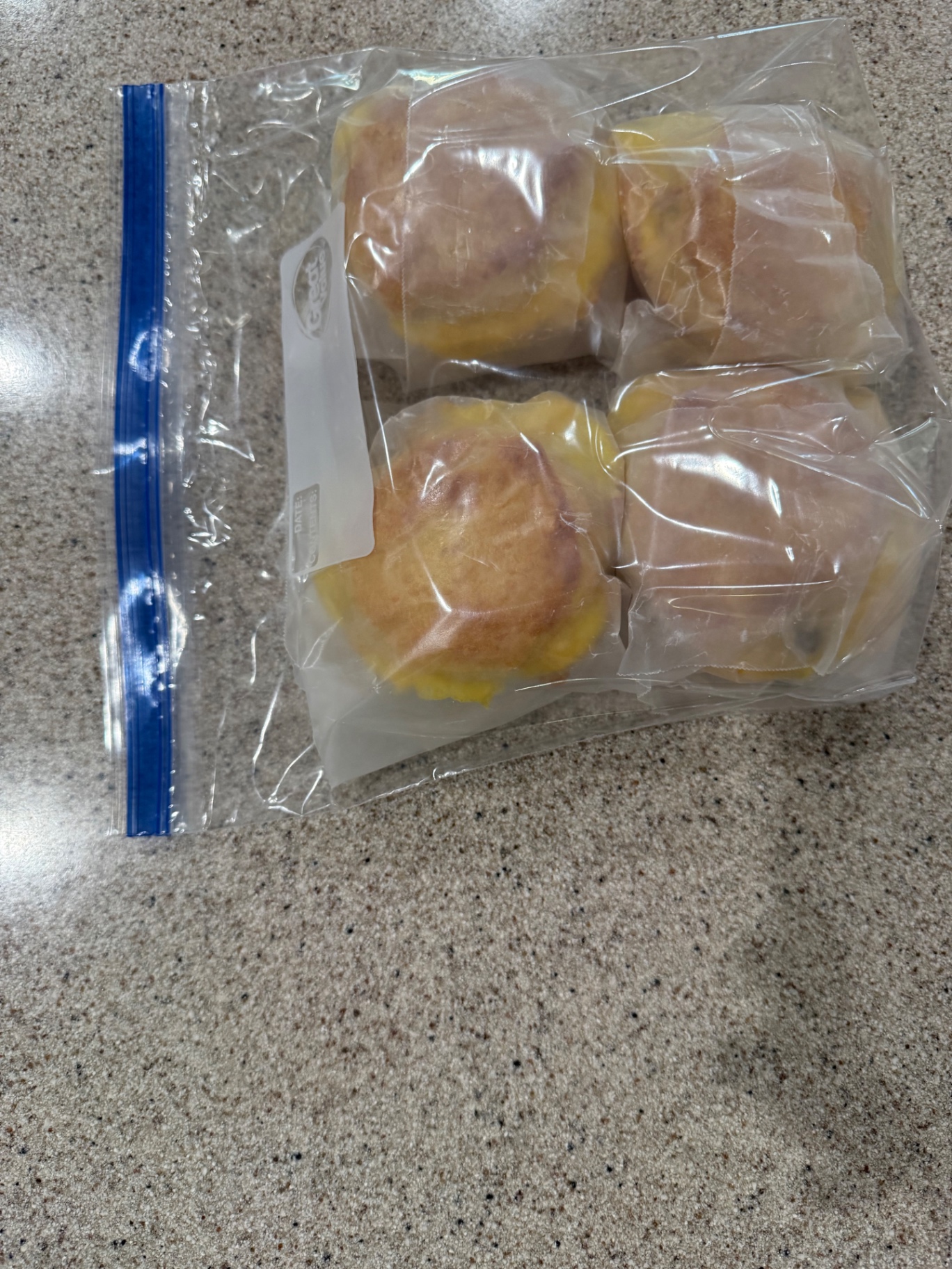 Cooked breakfast biscuits wrapped individually in parchment paper for refrigerator storage.