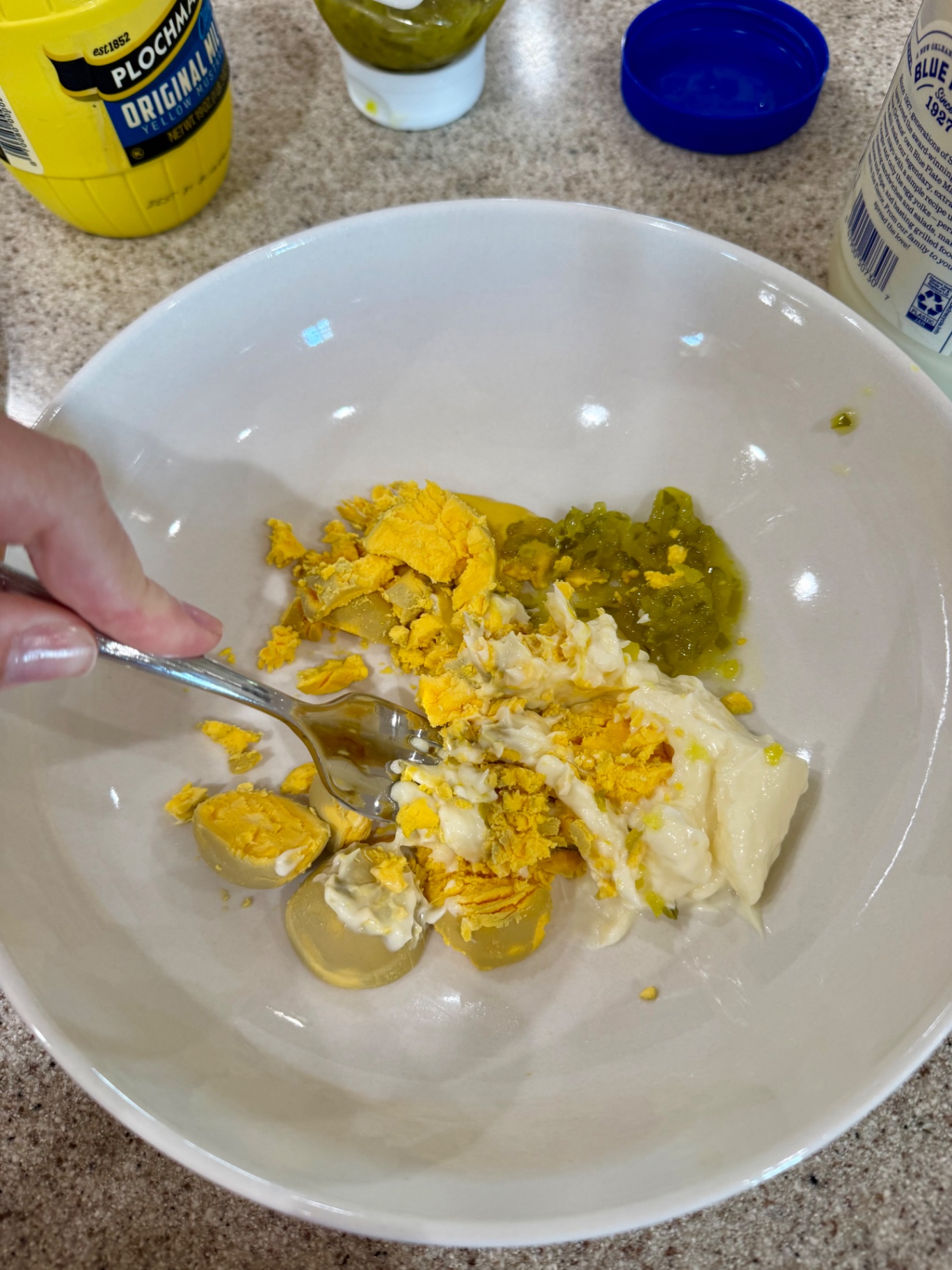 Using a fork to mash egg yolks with mayonnaise, mustard, and relish.