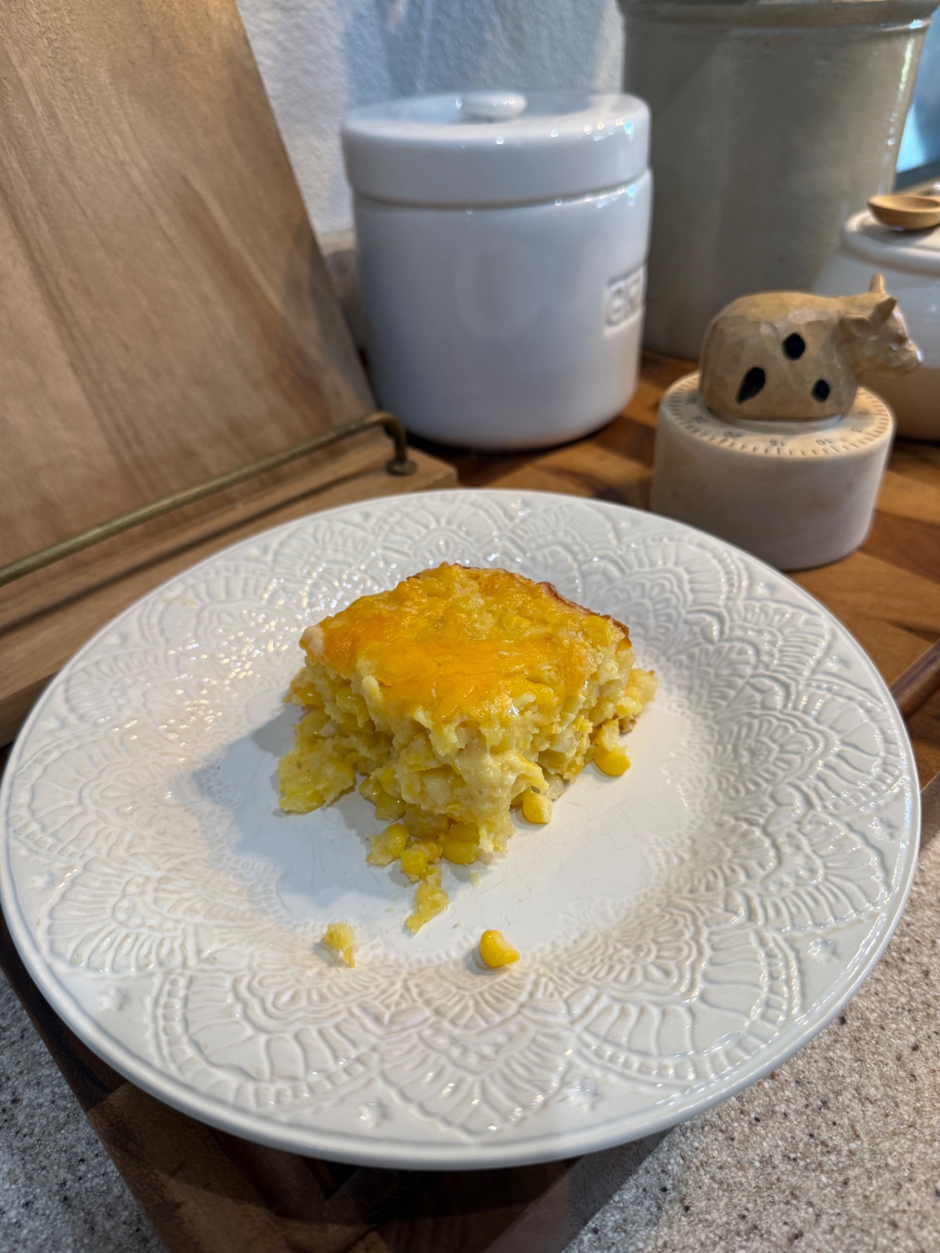 A serving of cheesy corn casserole on a white patterned plate in the Pasture Threads kitchen.