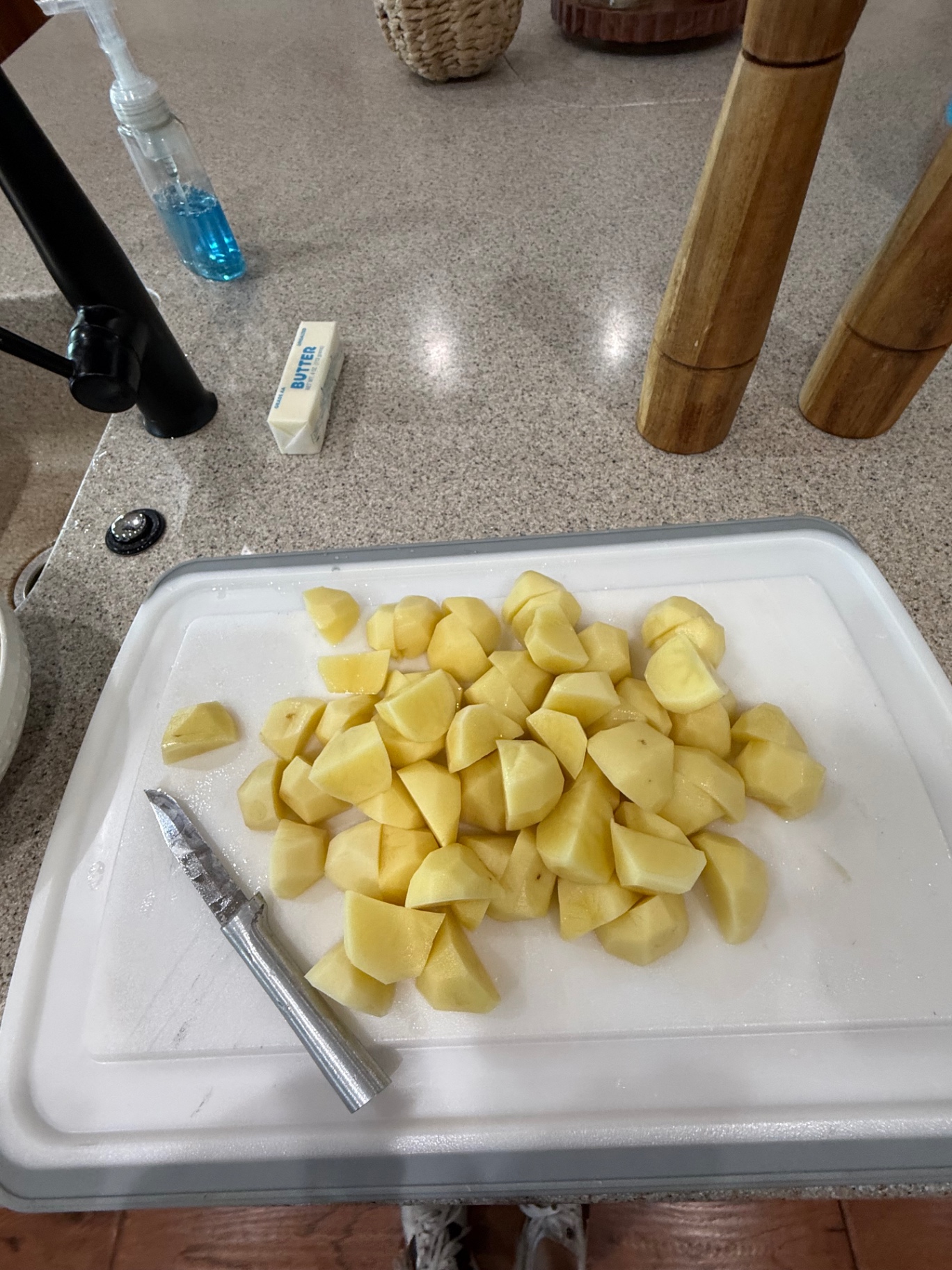 Peeled Yukon Gold potato chunks on a white cutting board beside a knife.