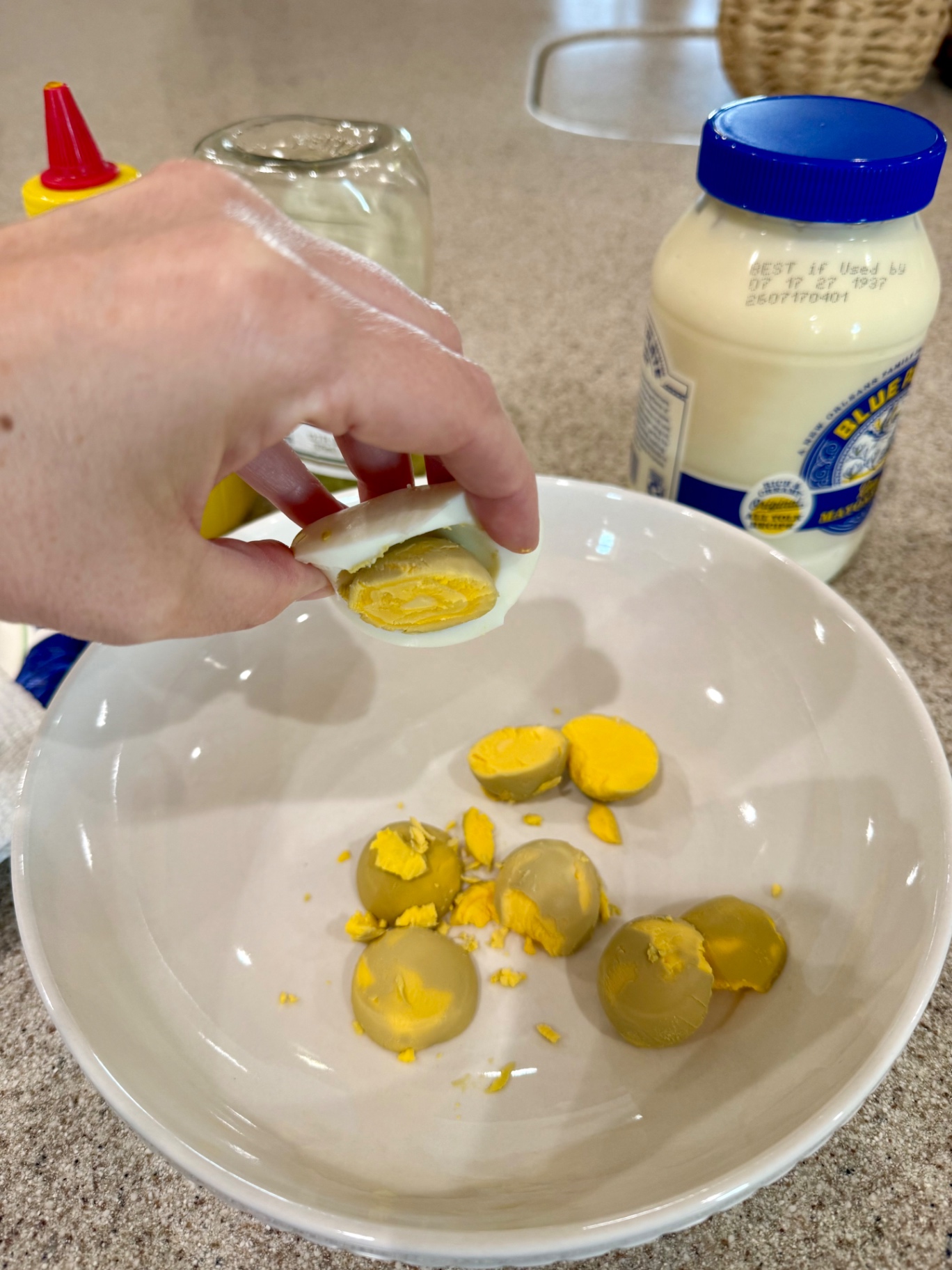 Removing an egg yolk from a halved egg white into a white mixing bowl.