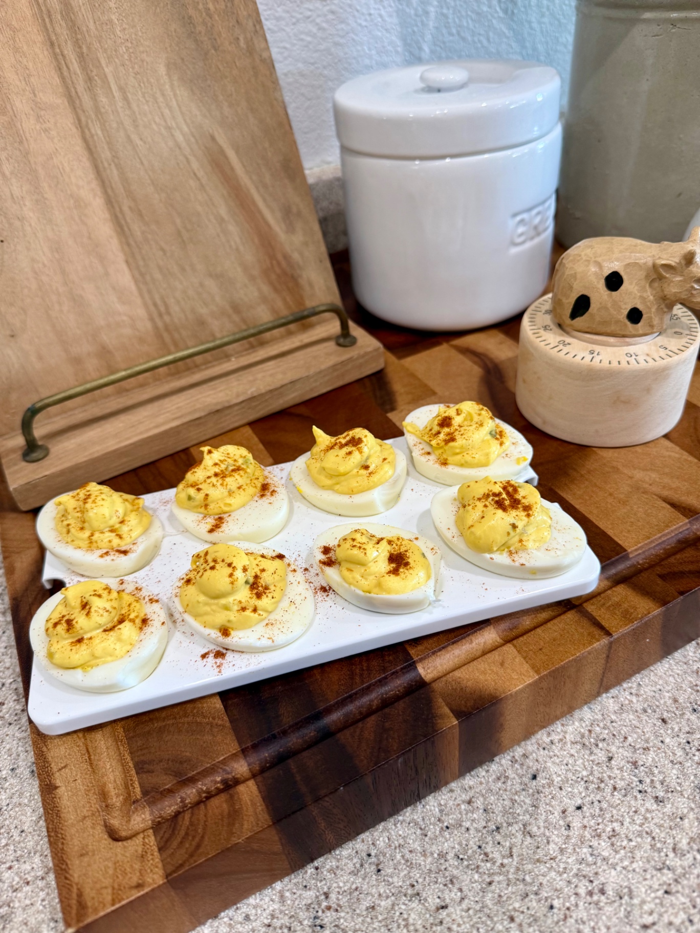Eight deviled egg halves topped with smoked paprika on a white serving tray on a wooden board.