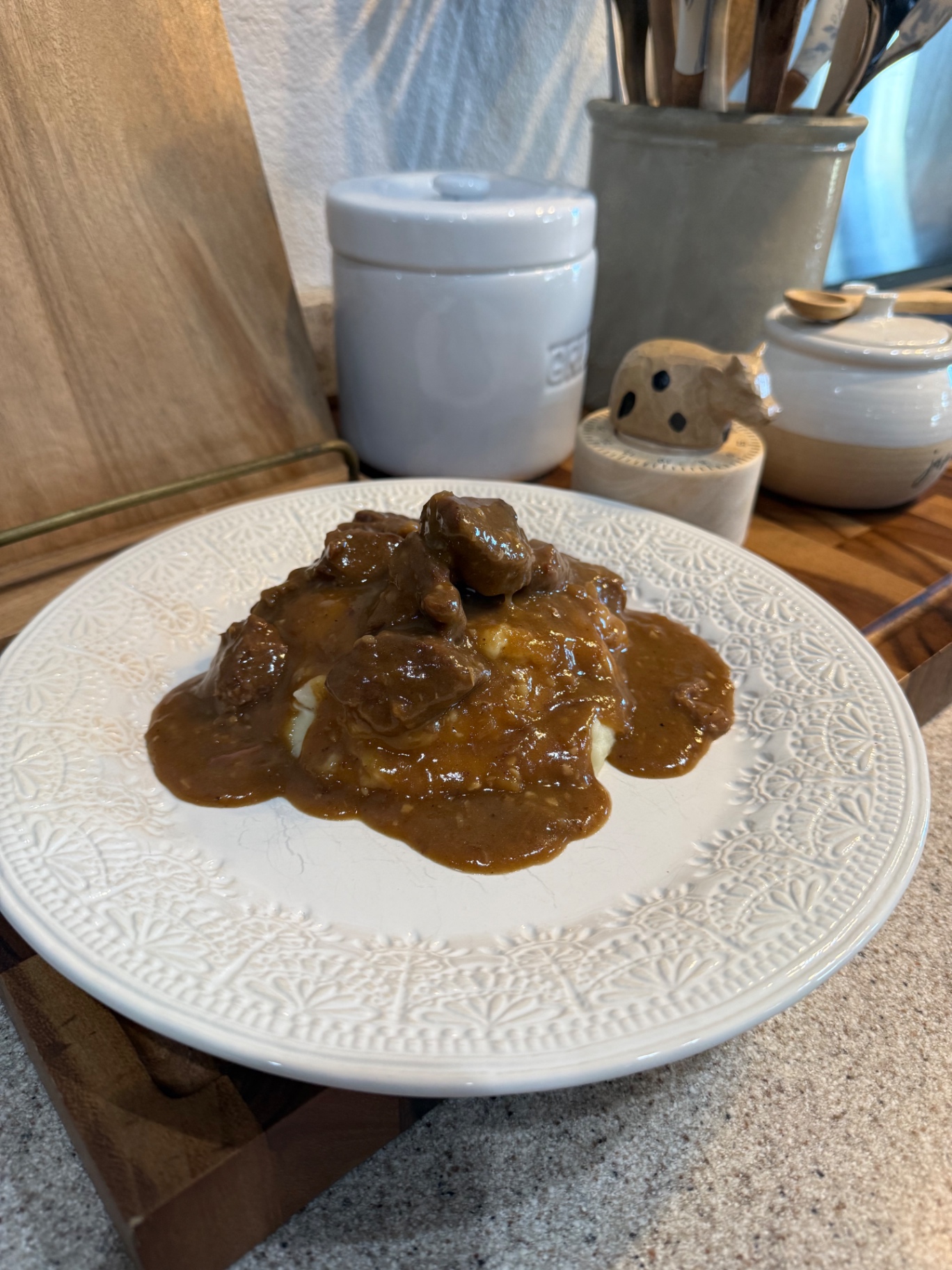 Beef tips with homemade gravy spooned over creamy mashed potatoes on a white patterned plate.