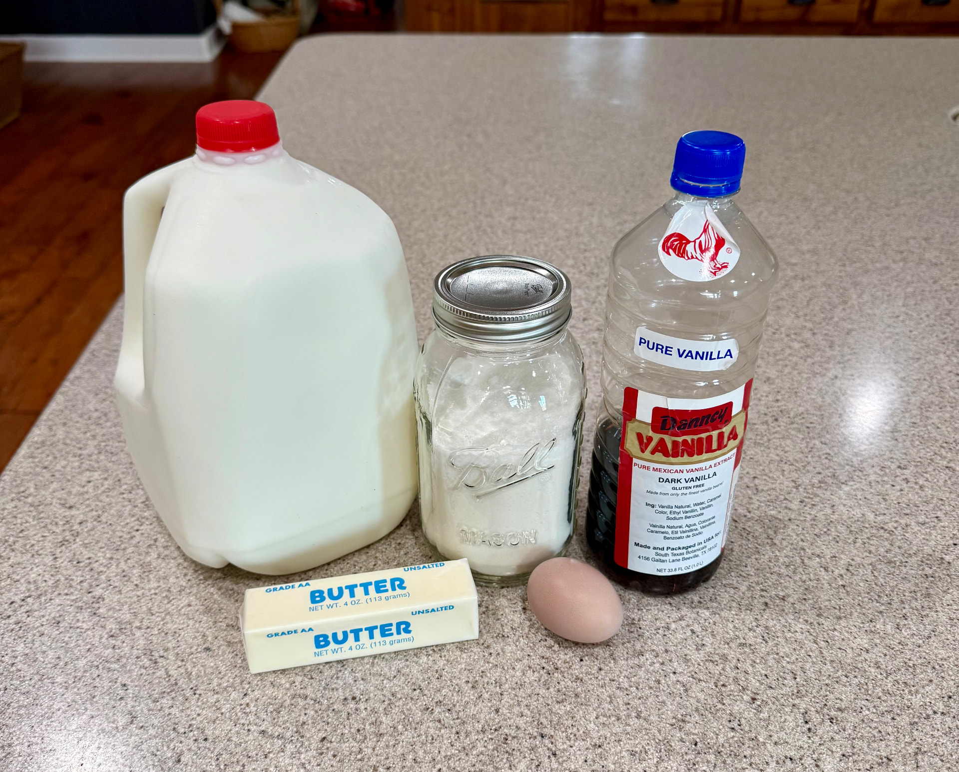 A filled quart jar of pancake mix beside whole milk, an egg, butter, and vanilla.