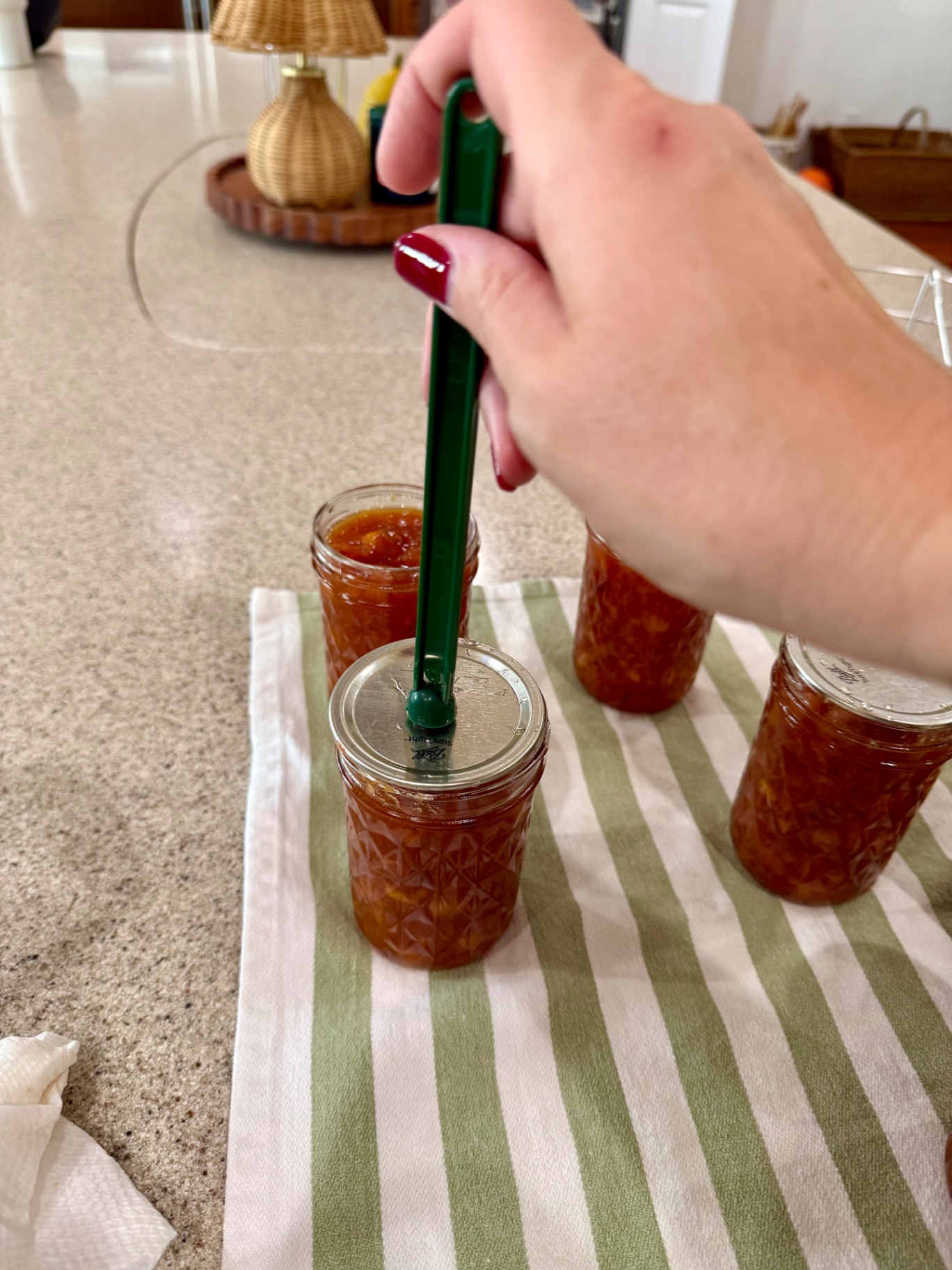 A canning lid being centered on a peach topping jar with a green magnetic lid lifter