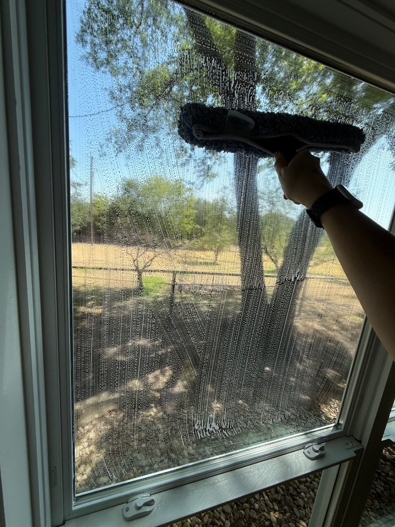 Scrubbing a soapy window with a microfiber window washer.