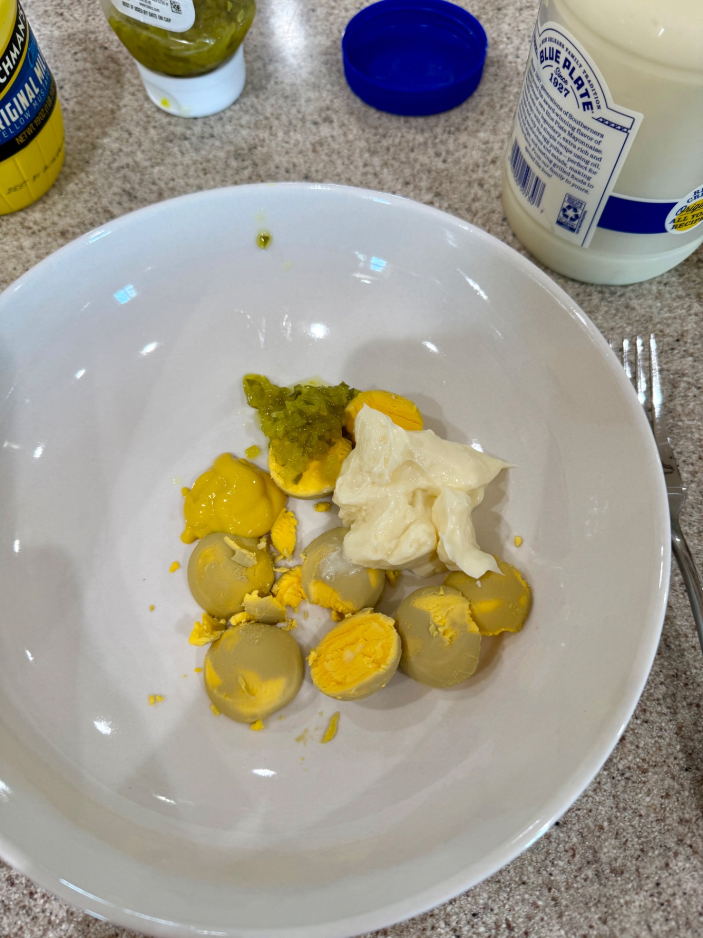 Cooked egg yolks with mayonnaise, yellow mustard, and sweet pickle relish in a white bowl.