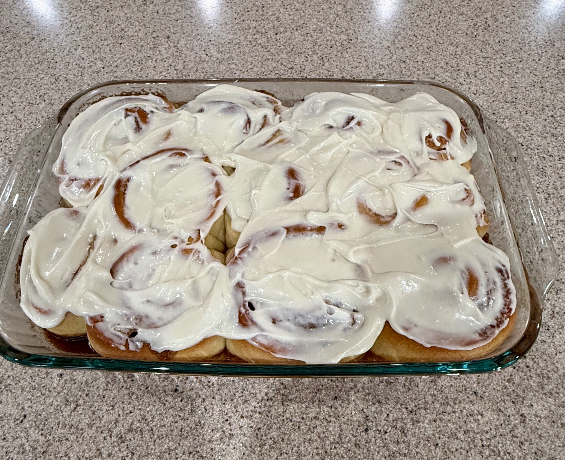 A glass baking dish of warm cinnamon rolls spread thick with cream cheese frosting