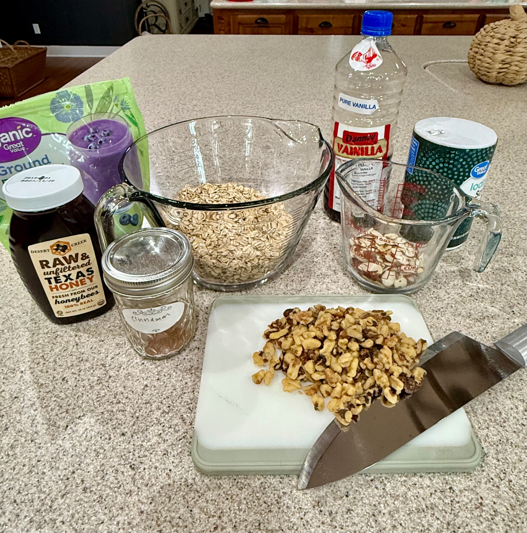 Granola ingredients on the counter: rolled oats, chopped walnuts, sliced almonds, ground flaxseed, honey, cinnamon, vanilla, and salt.